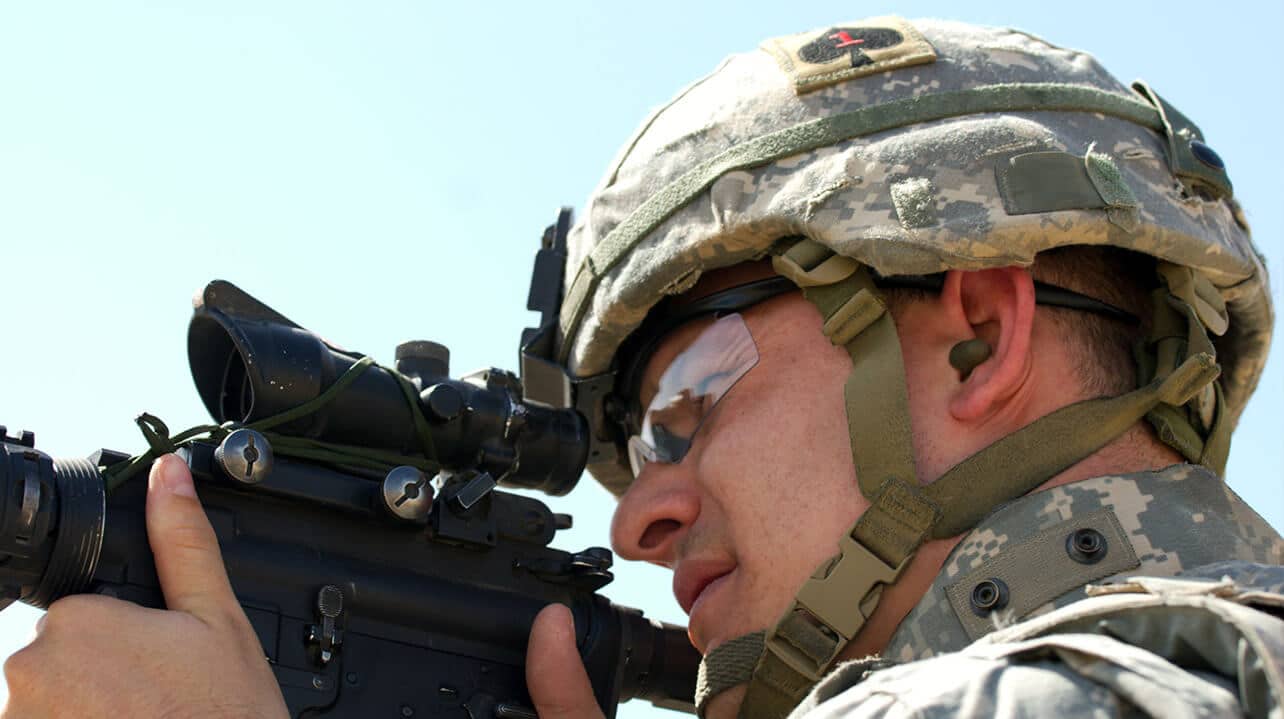 military man with earplugs in aiming rifle